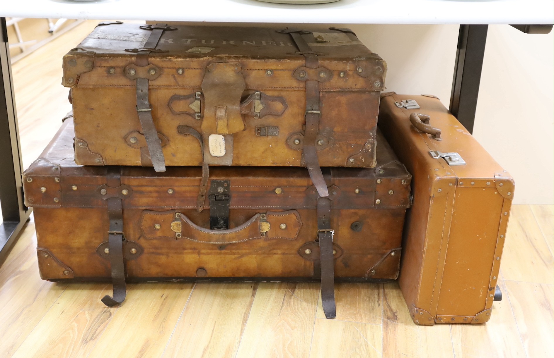 Three early 20th century brown leather cabin trunks and a later vintage suitcase, largest trunk 92cms wide x 52cms deep